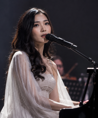 Isyana Sarasvati tampil memainkan piano di atas panggung konser dengan pencahayaan artistik dan suasana megah