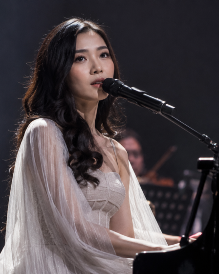Isyana Sarasvati tampil memainkan piano di atas panggung konser dengan pencahayaan artistik dan suasana megah