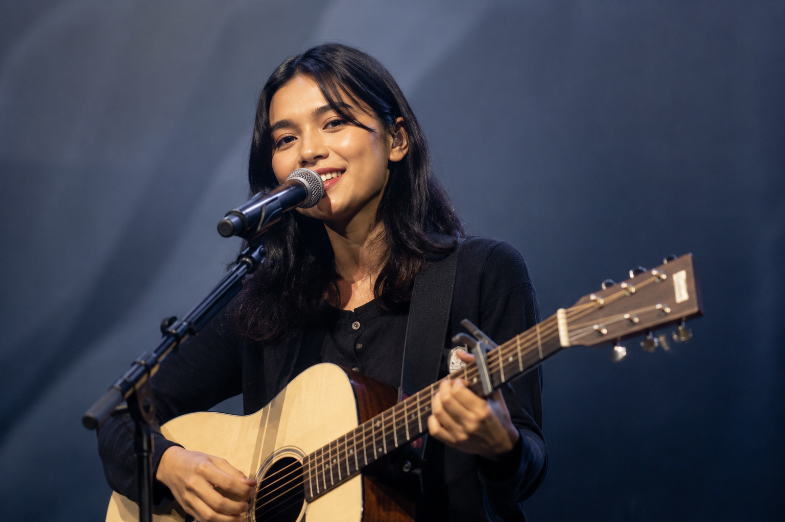 Feby Putri tampil membawakan lagu di atas panggung dengan gitar akustik dan pencahayaan hangat