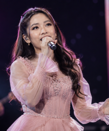 Tiara Andini tampil membawakan lagu di atas panggung konser dengan pencahayaan profesional dan penonton memenuhi area pertunjukan