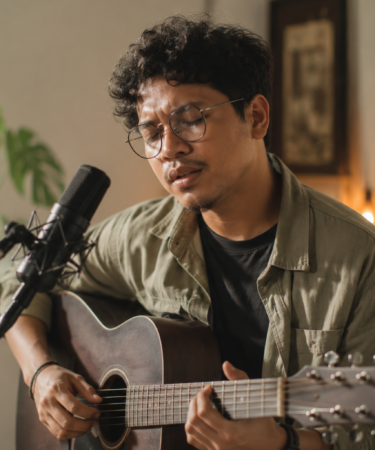 Budi Doremi tampil bernyanyi di atas panggung dengan gitar akustik dan pencahayaan konser yang hangat