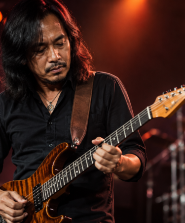 Dewa Budjana memainkan gitar elektrik saat tampil di atas panggung konser musik