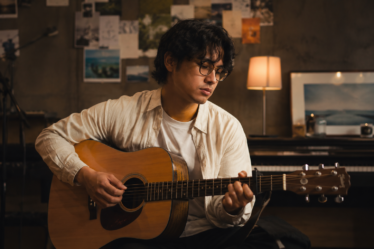 Bilal Indrajaya tampil membawakan lagu di atas panggung dengan gitar akustik dan pencahayaan konser yang hangat