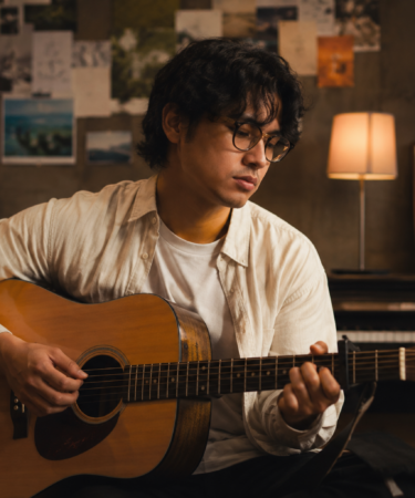 Bilal Indrajaya tampil membawakan lagu di atas panggung dengan gitar akustik dan pencahayaan konser yang hangat