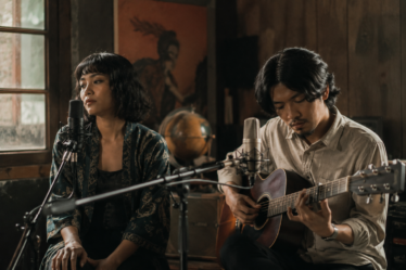 Banda Neira tampil membawakan lagu folk di atas panggung dengan gitar akustik dan pencahayaan hangat