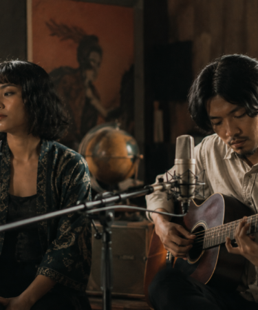 Banda Neira tampil membawakan lagu folk di atas panggung dengan gitar akustik dan pencahayaan hangat