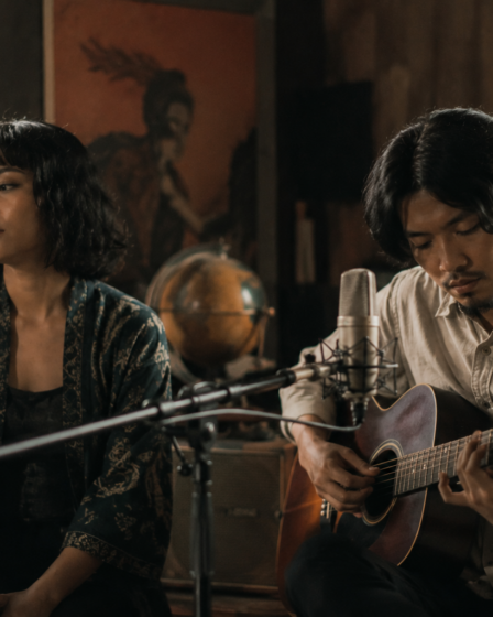 Banda Neira tampil membawakan lagu folk di atas panggung dengan gitar akustik dan pencahayaan hangat