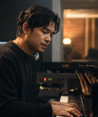 Musisi Petra Sihombing tampil di atas panggung sambil memainkan gitar dengan pencahayaan konser yang hangat.